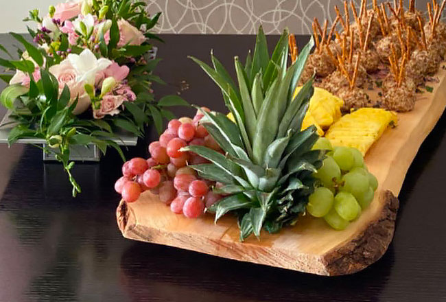 Fruit on board with flowers on a table.